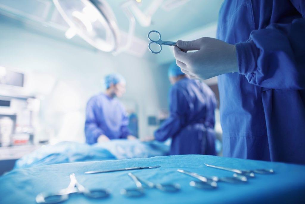 A surgeon in scrubs holds a pair of scissors